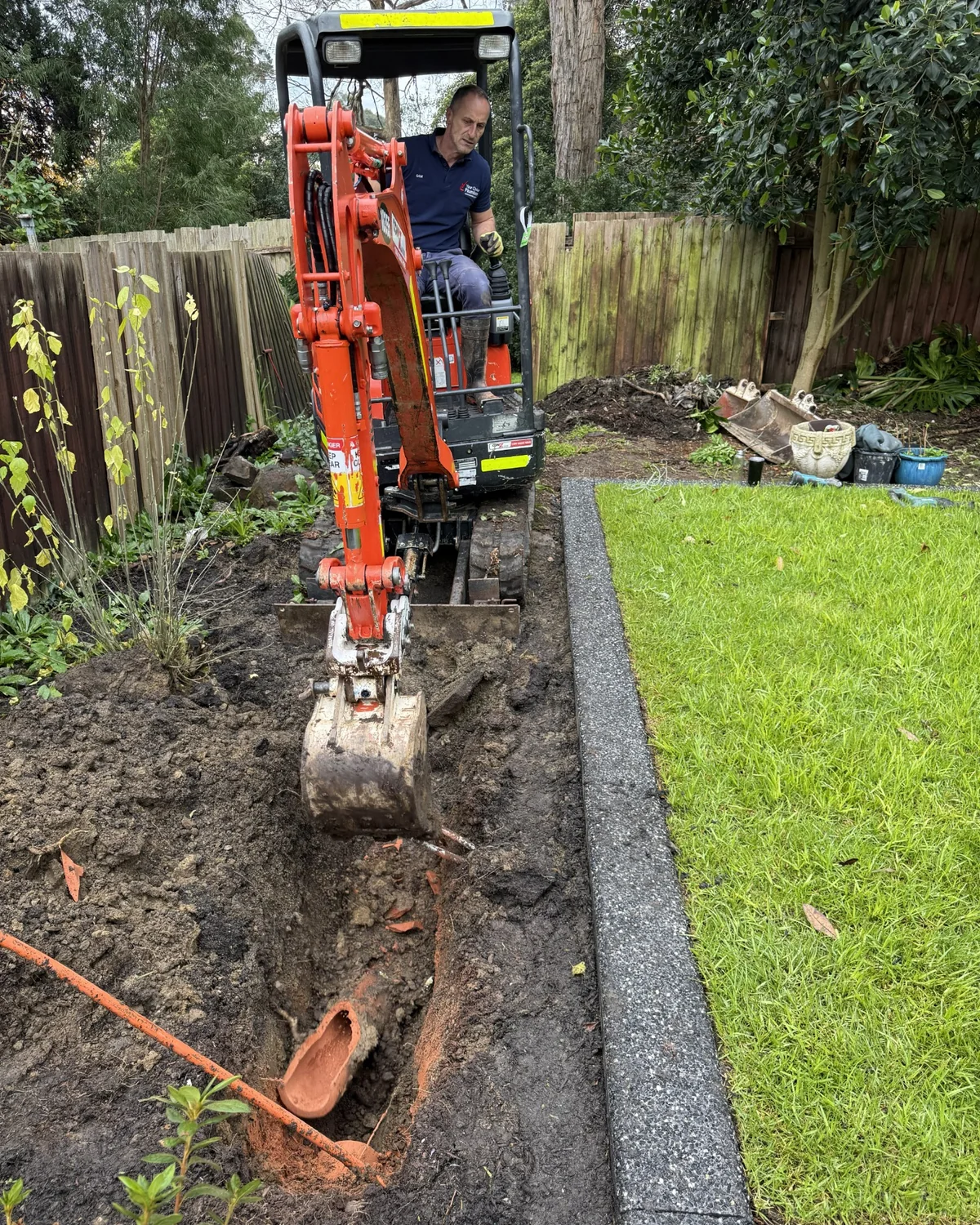 Plumber excavating around a damaged underground stormwater drain with a mini excavator.