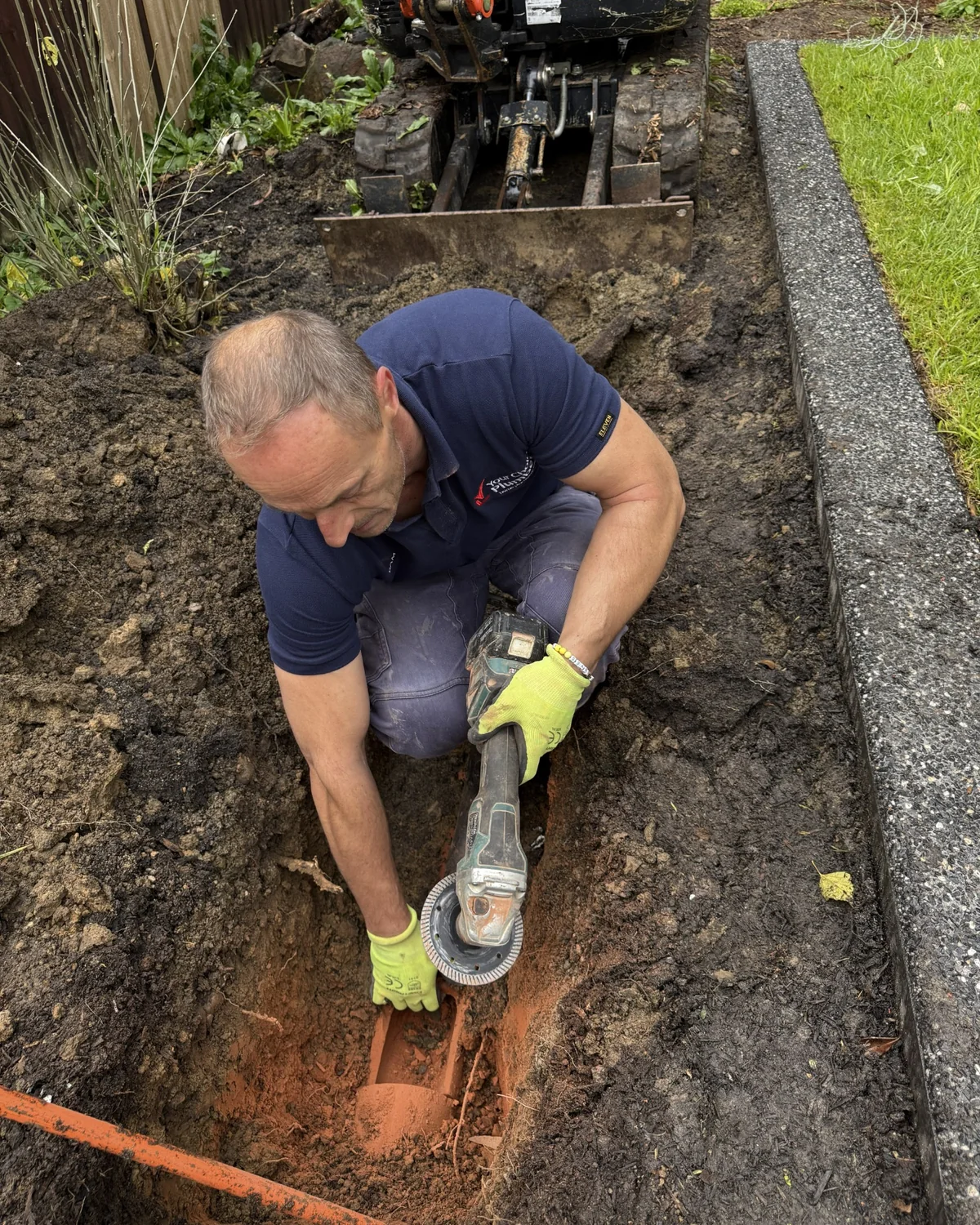 Plumber cutting and removing an old terracotta stormwater drain during excavation.