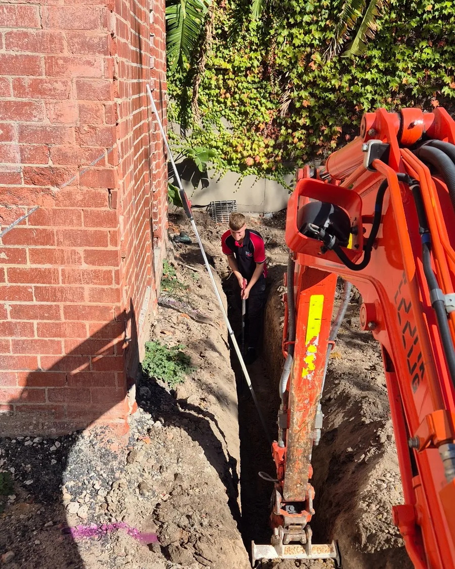 Excavated trench beside a house for underground sewer drain replacement.
