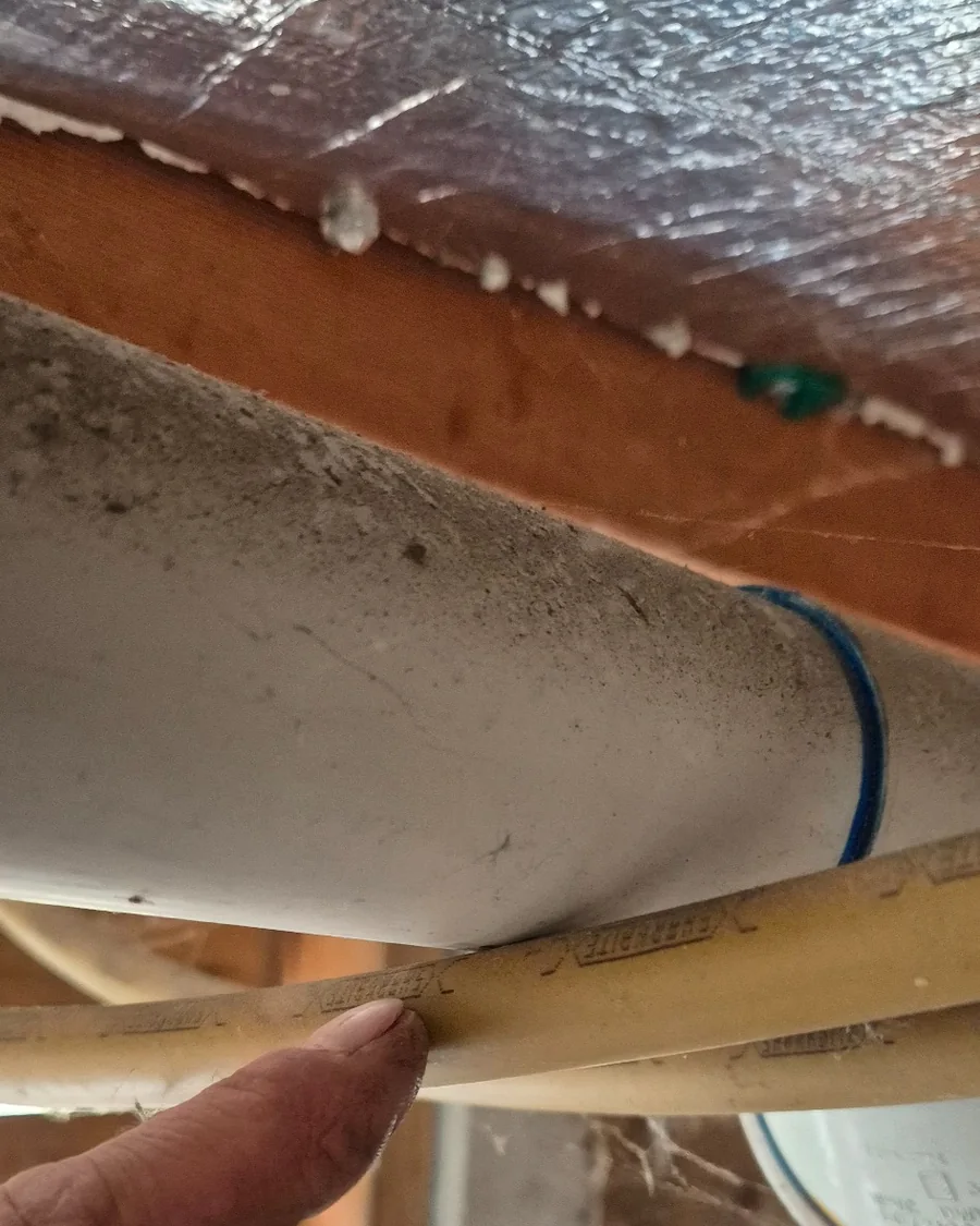 Water pipe contacting surrounding materials under a house, contributing to pipe vibration and water hammer noise.