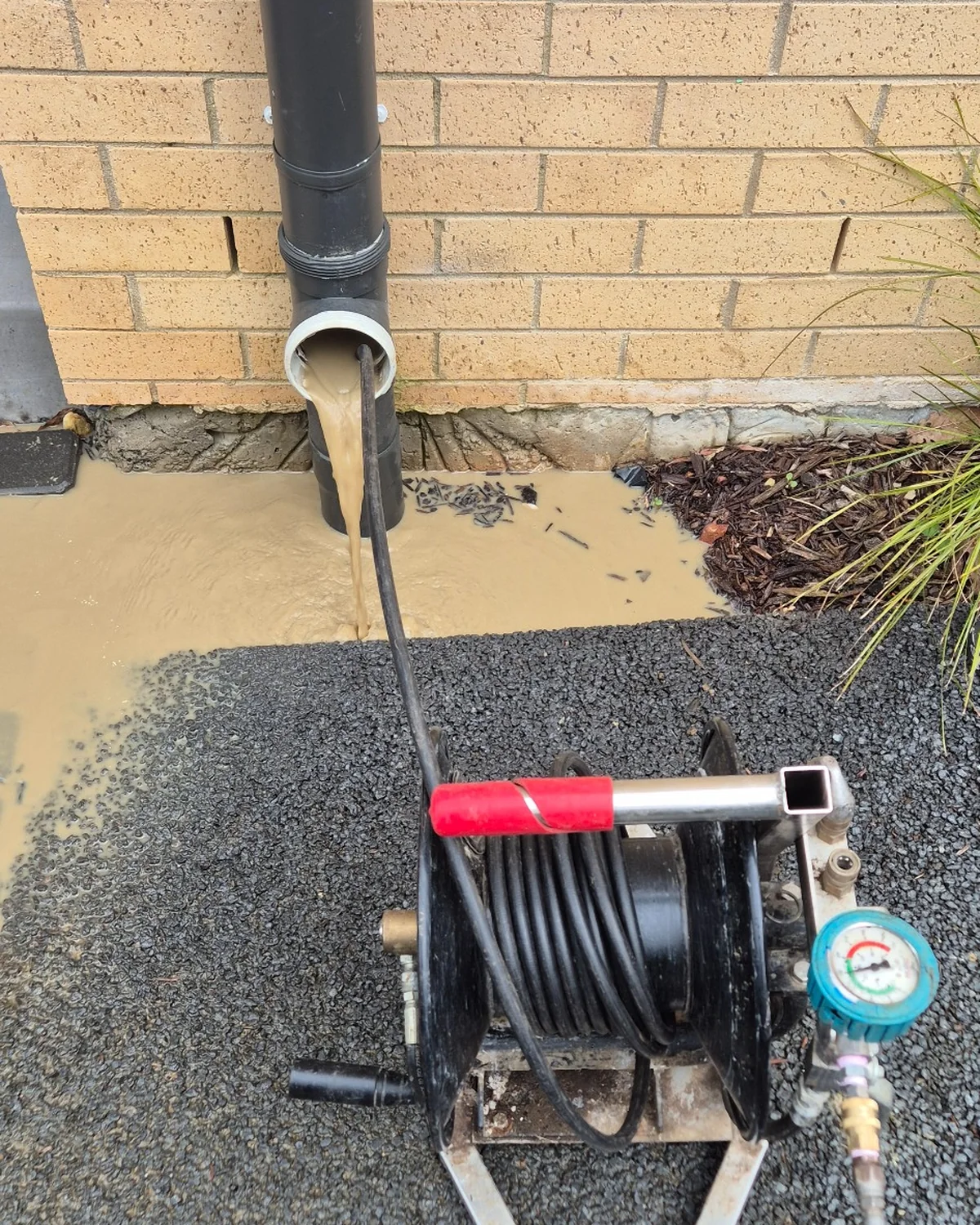 Blocked stormwater downpipe overflowing with muddy water while high-pressure hydro jetting equipment is used to clear the drain.