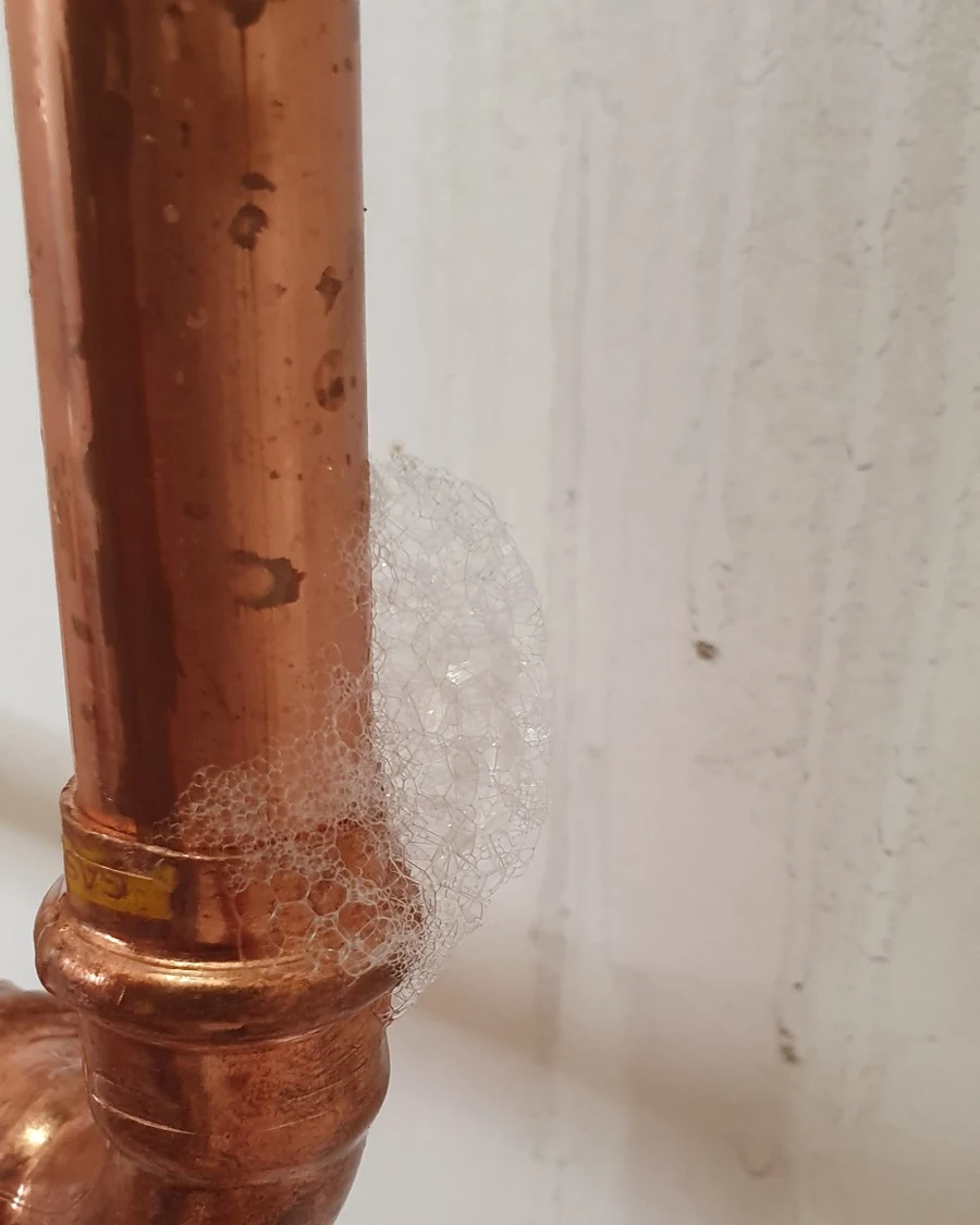 Leak detection bubbles forming around a copper gas pipe fitting during residential gas leak testing.