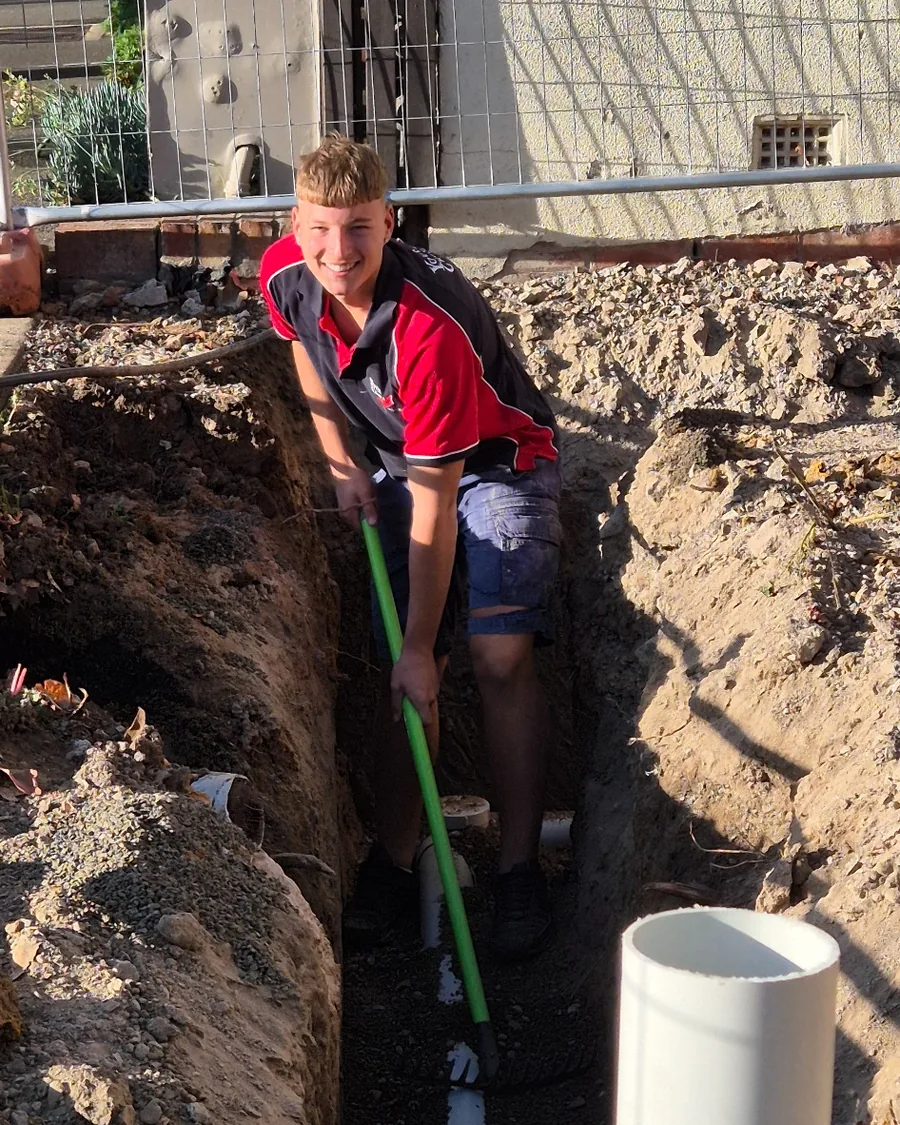 Plumber installing and bedding new sewer pipe in an excavated trench.