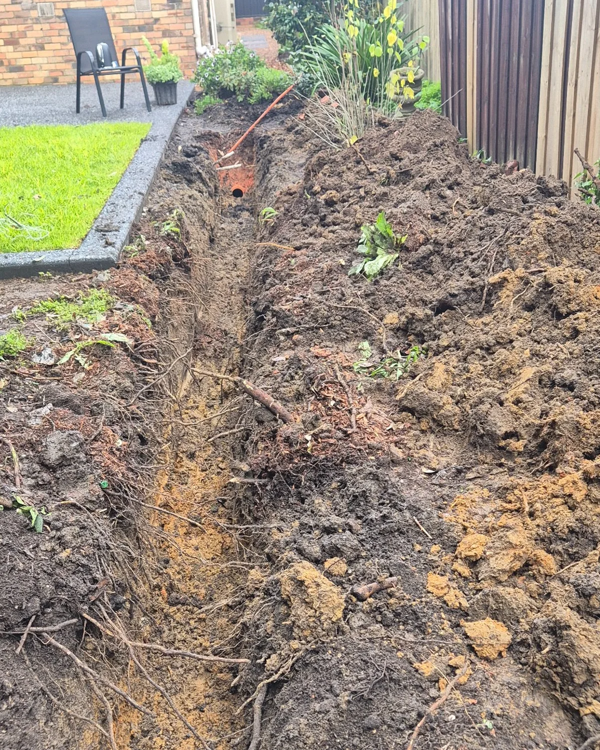 Long excavated trench through a backyard for underground stormwater drain replacement.