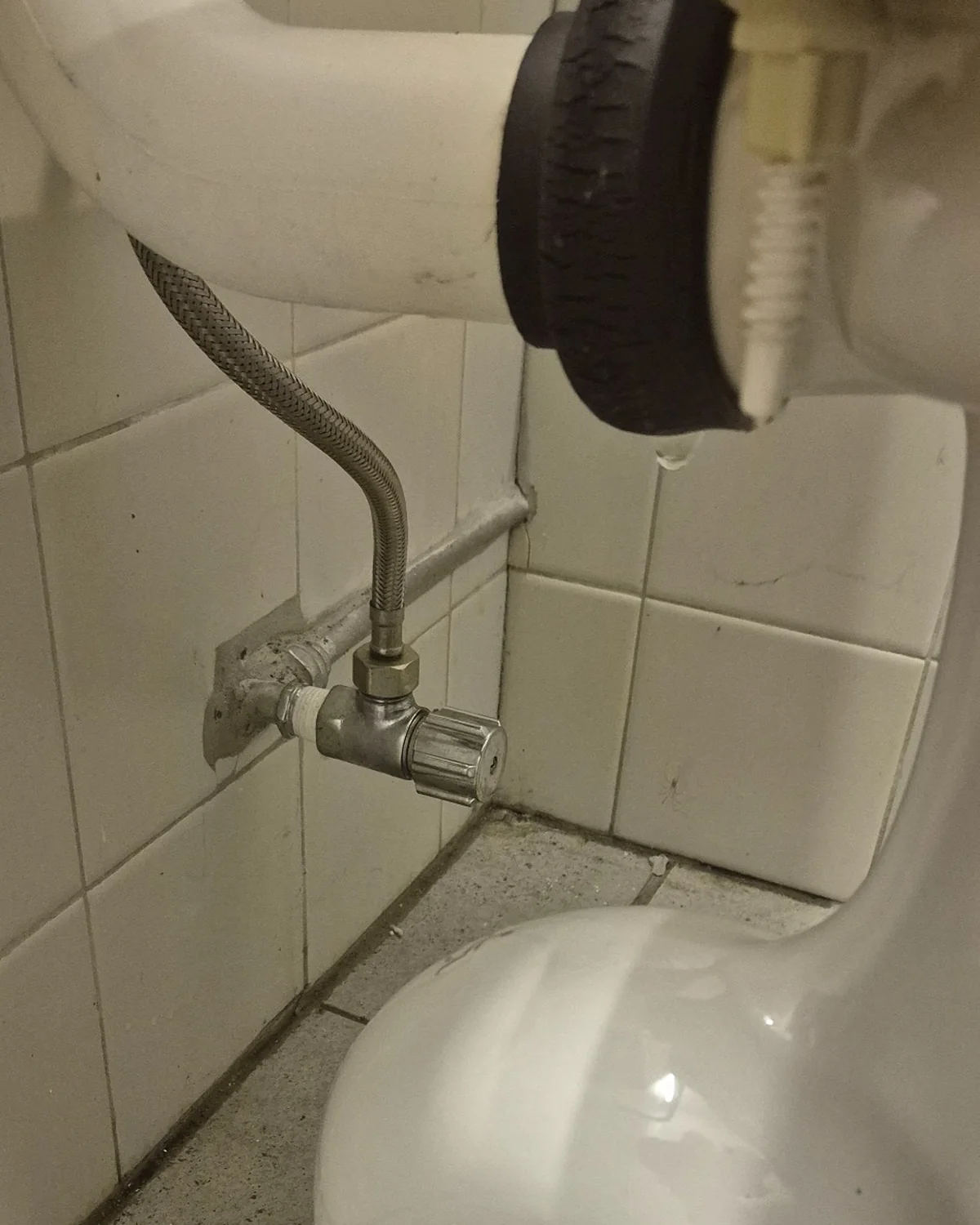 Close-up of a leaking toilet flush pipe connector rubber showing visible deterioration and a water droplet forming at the connection.