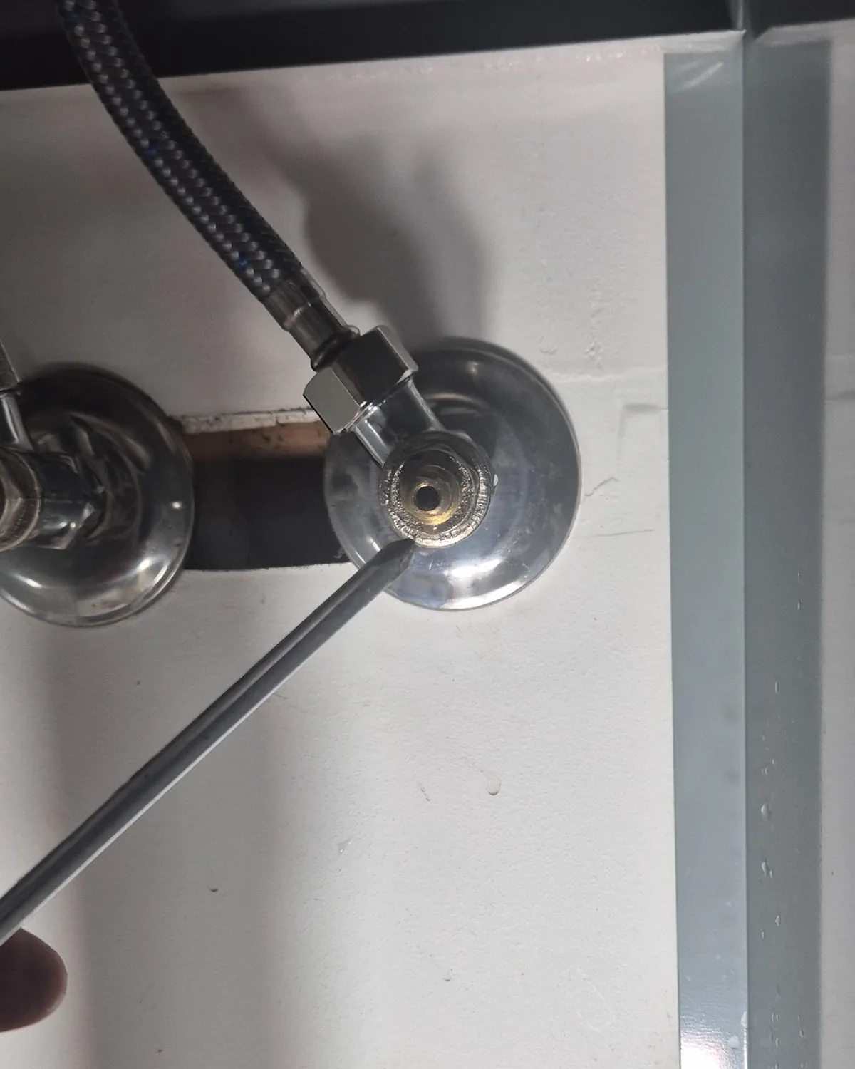 Plumber inspecting a leaking isolation valve connection inside a household cupboard.
