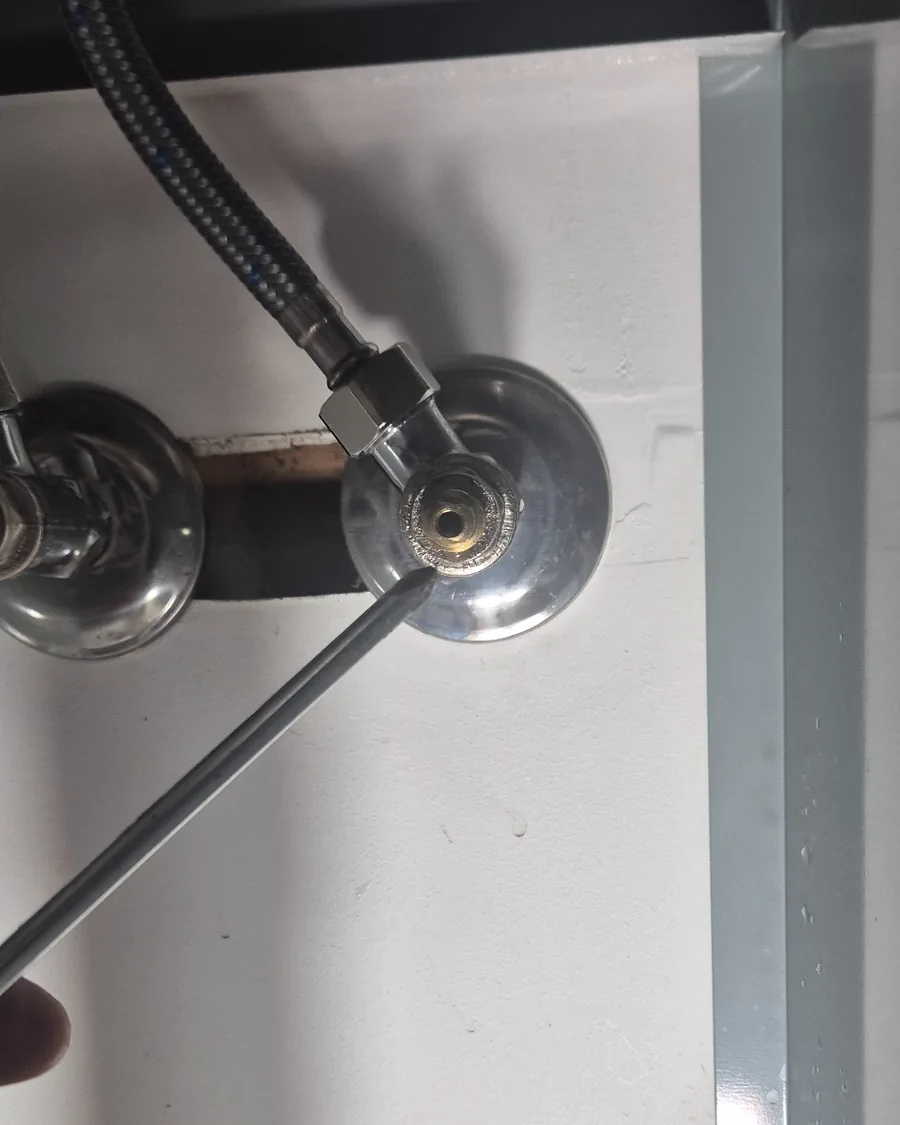 Plumber inspecting a leaking isolation valve connection inside a household cupboard.