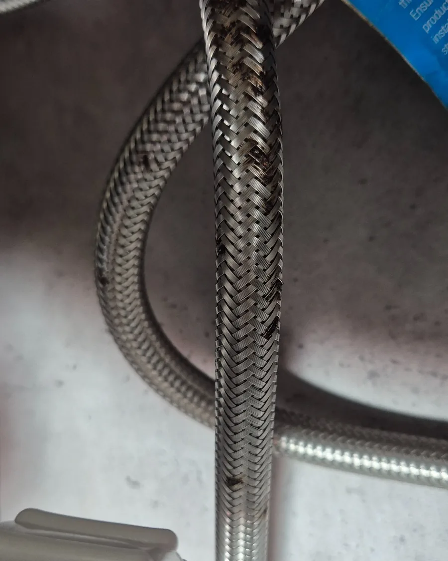 Corrosion and tea-staining developing along an ageing flexible hose beneath a sink.