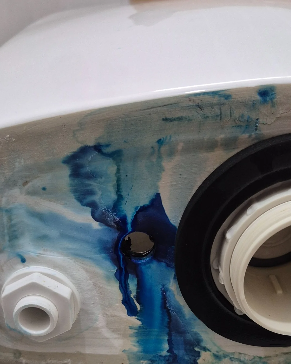 Inside a toilet cistern showing the outlet area during diagnosis of a leaking toilet fault.