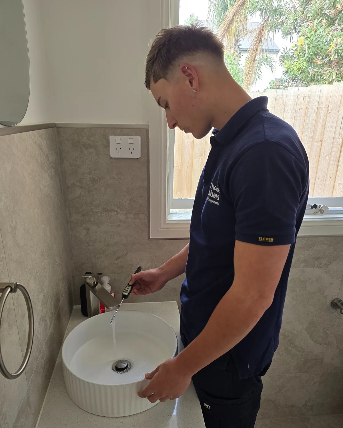 Your Choice Plumbers plumber checking hot water temperature at a bathroom basin using a digital thermometer.
