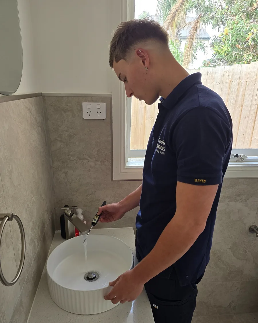 Your Choice Plumbers plumber checking hot water temperature at a bathroom basin using a digital thermometer.