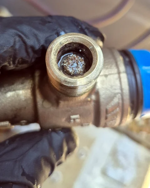 Close-up of a blocked tempering valve strainer with debris and build-up.