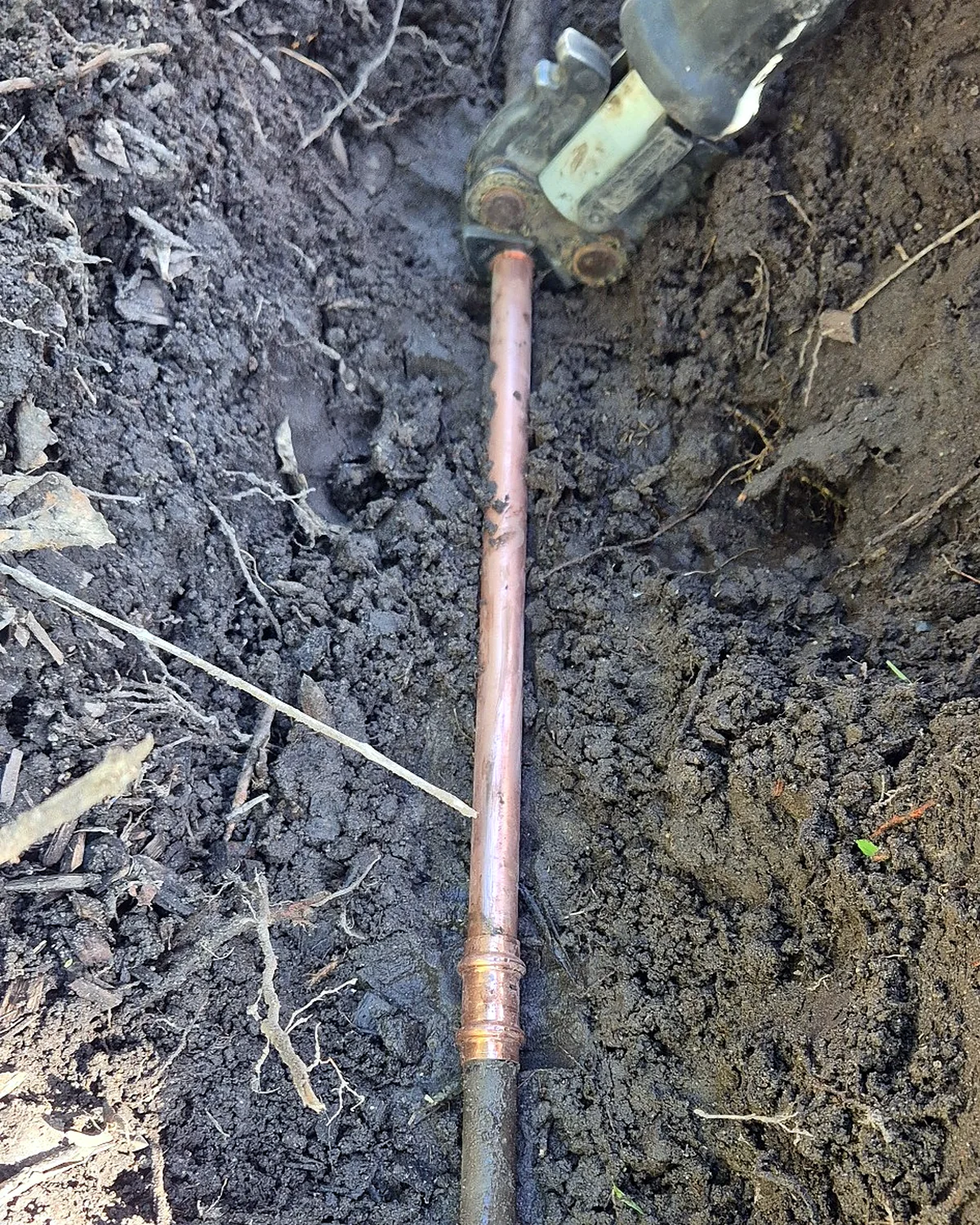 New copper pipe installed in a trench during a burst water pipe repair.