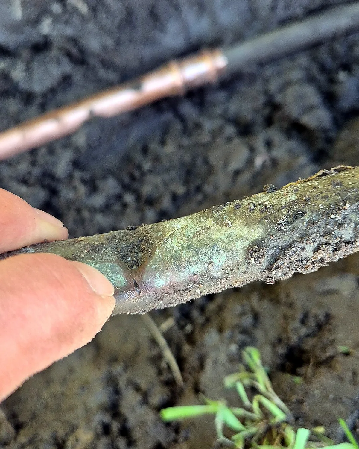 Burst copper pipe close-up with repaired copper water pipe visible in the background.